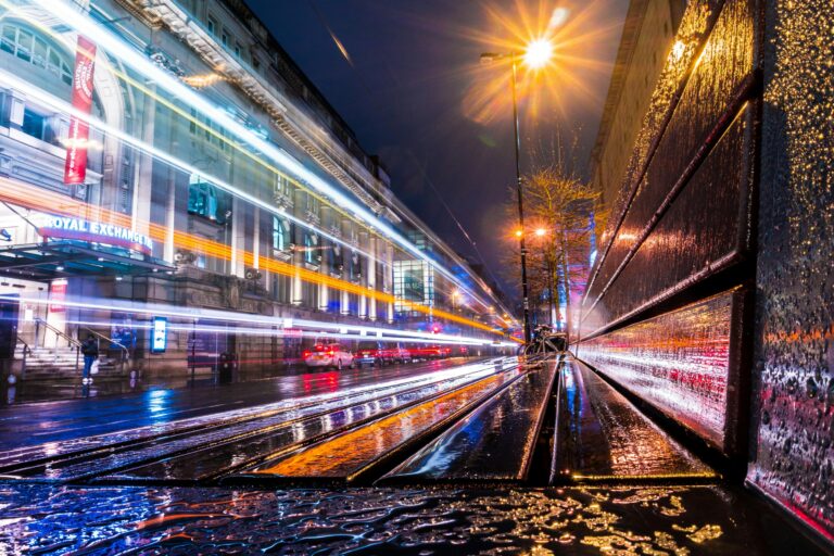 Night-time view of Manchester’s Royal Exchange with light trails from passing traffic reflecting on wet streets